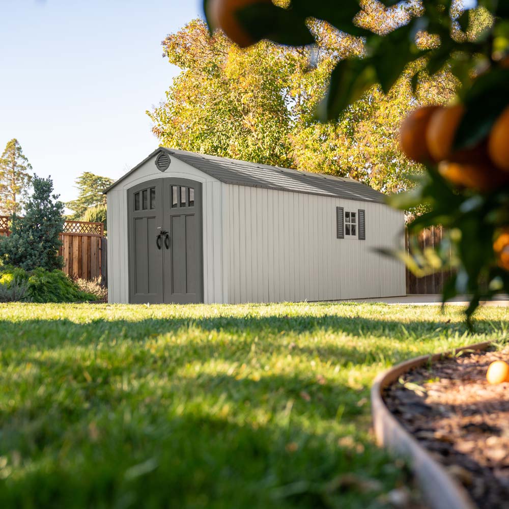Lifetime 8x20 shed in a backyard with a tall fence standing on a pavement. 