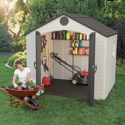 Woman gardening with a wheelbarrow next to the Lifetime 8x5 ft. storage shed with open doors and tool shelving visible.